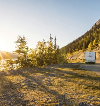 An RV driving a mountain highway at sunset, sunlight flaring through the trees.